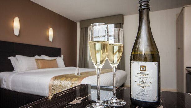 A hotel room with a bed, a nightstand, and a bottle of wine on a table. - Hotel Northbridge (Perth)