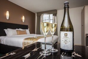 Une chambre d’hôtel avec un lit, une table de chevet et une bouteille de vin posée sur une table.