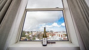 A bottle of wine and a glass on a windowsill, with a view of buildings and a cloudy sky. - Hotel Northbridge (Perth)
