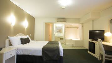 A hotel room with a bed, bedside table, desk with a chair, a television, and a bathroom with a shower and sink.