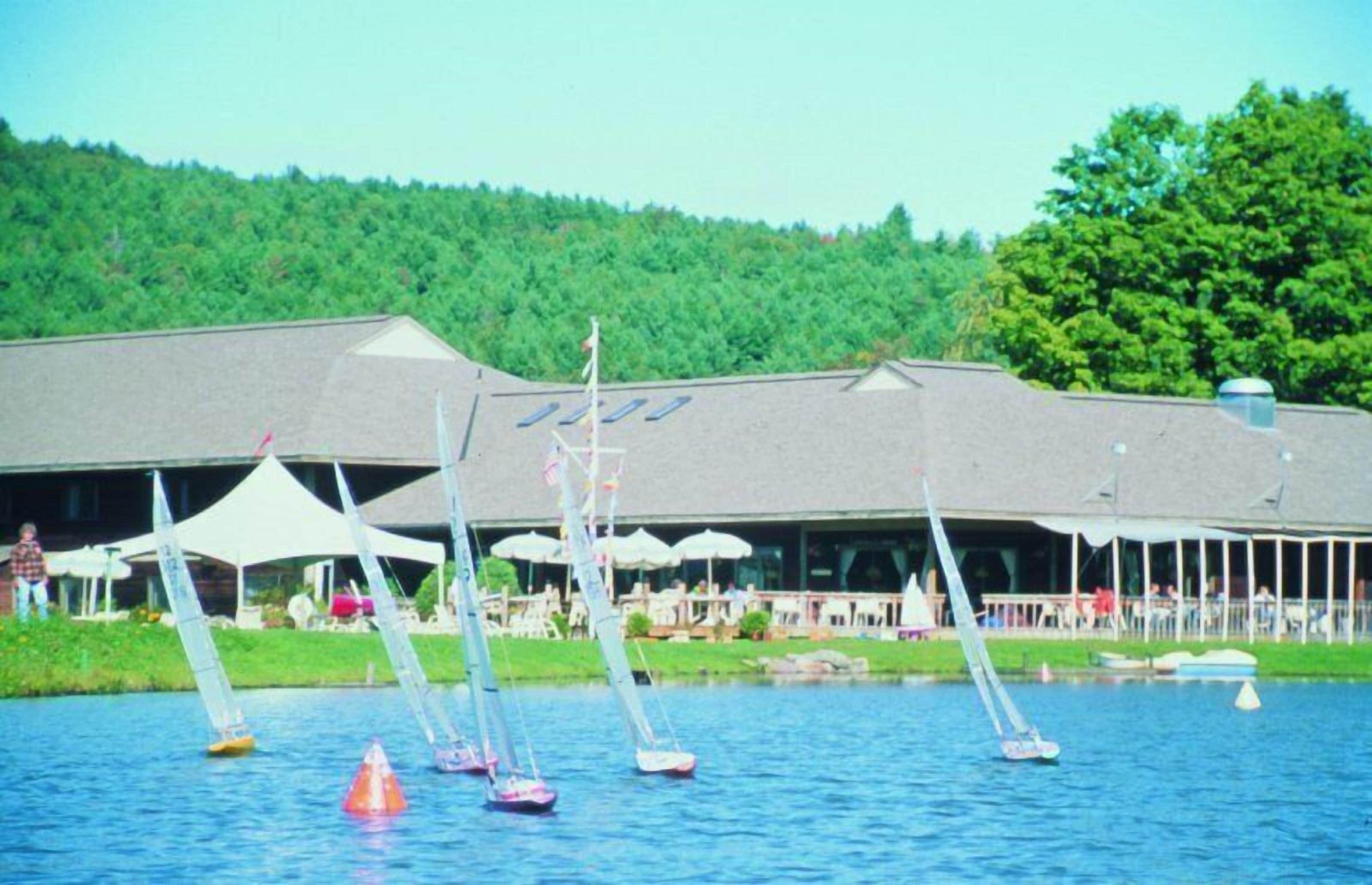 A lakeside building with multiple sailboats on the water.