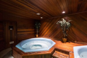 Interior de una cabaña de madera con jacuzzi, paredes de madera y techo con vigas de madera.