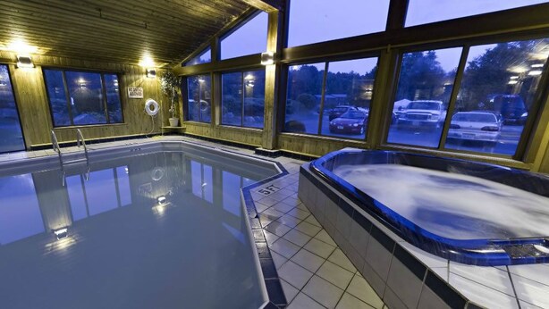Ein Hallenbad mit Whirlpool, Holzverkleidung und großen Fenstern.
