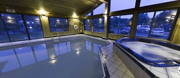 Piscina interior con hidromasaje, paredes de madera y ventanas grandes.