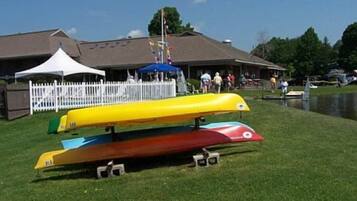 A row of colorful canoes on a grassy area with a building and a fence in the background.