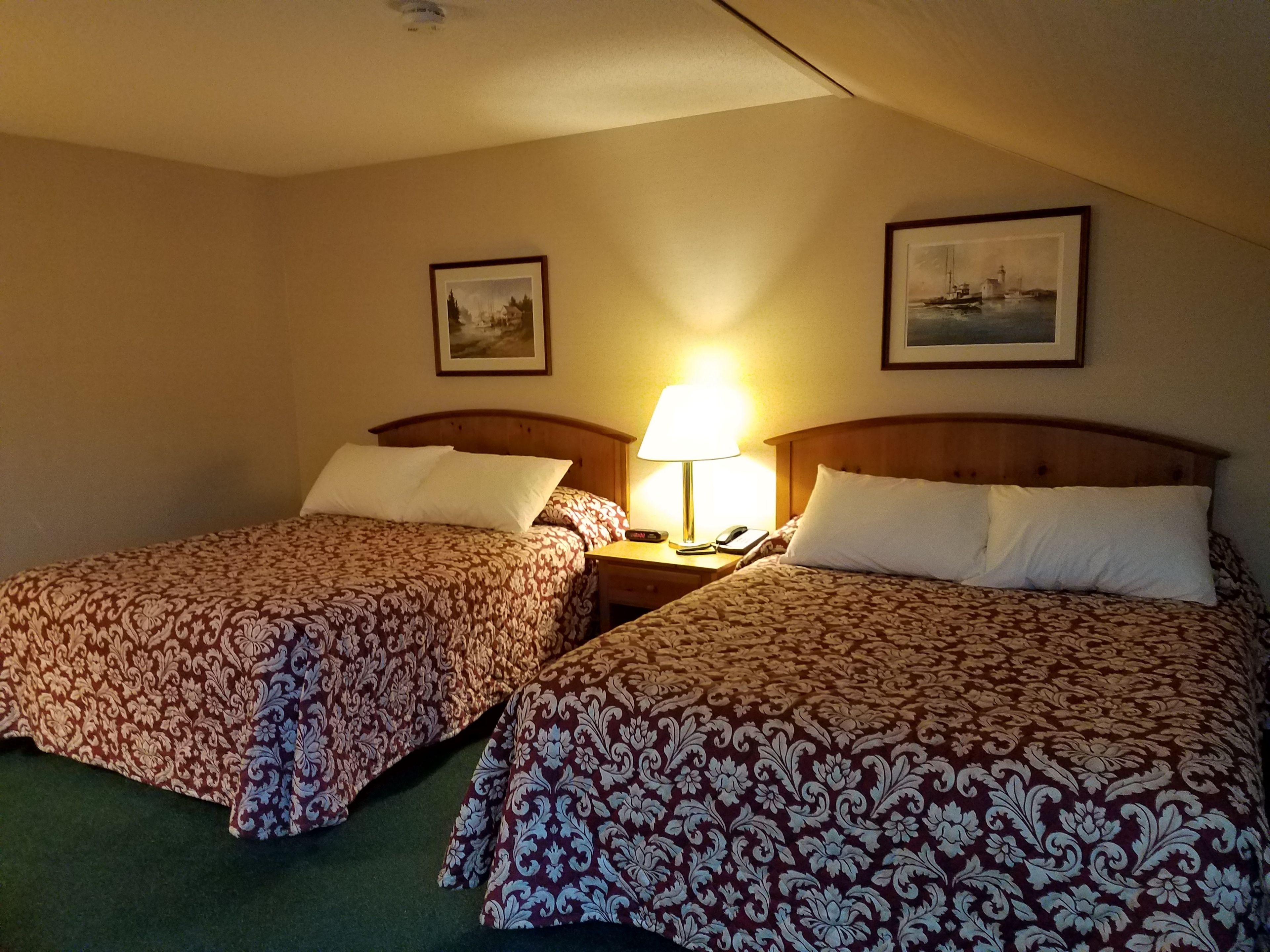 Een hotelkamer met twee bedden, elk voorzien van beddengoed met een patroon, een nachtkastje met een lamp, en twee ingelijste foto’s aan de muur.