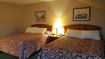 Een hotelkamer met twee bedden, elk voorzien van beddengoed met een patroon, een nachtkastje met een lamp, en twee ingelijste foto’s aan de muur.
