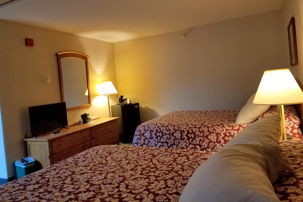 A hotel room with two beds, a desk with a lamp, a television, and a mirror.