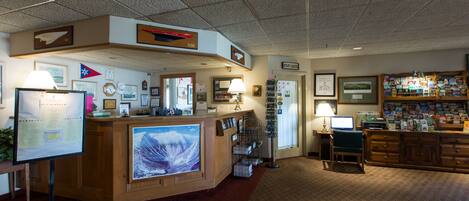 A reception area with a wooden desk, a large monitor, framed pictures, and a carpeted floor.