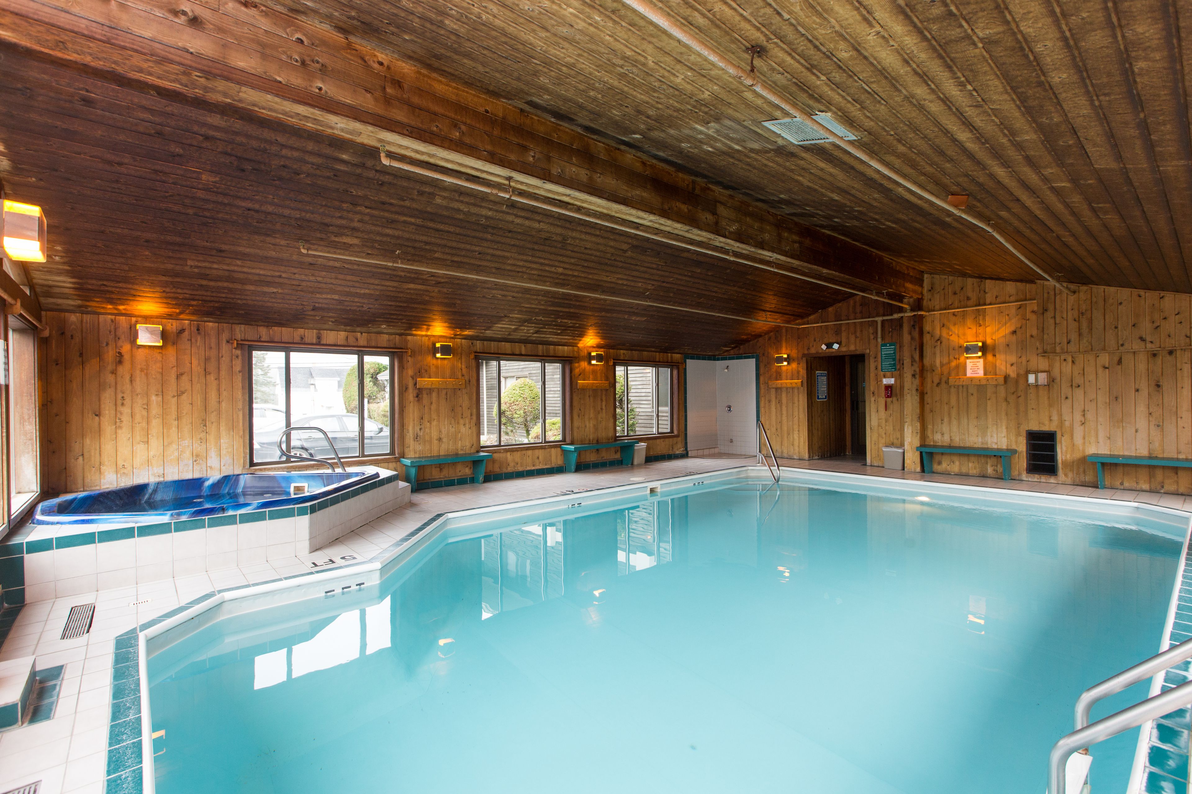An indoor swimming pool with a hot tub, wooden walls, and benches along the sides.