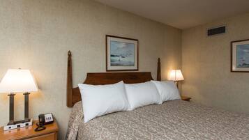 A hotel room with a bed, two bedside lamps, a nightstand with a phone, and two framed pictures on the wall.