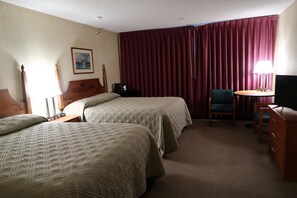 A hotel room with two beds, a desk, a chair, a TV, and a window with curtains. - Commodores Inn (Stowe)