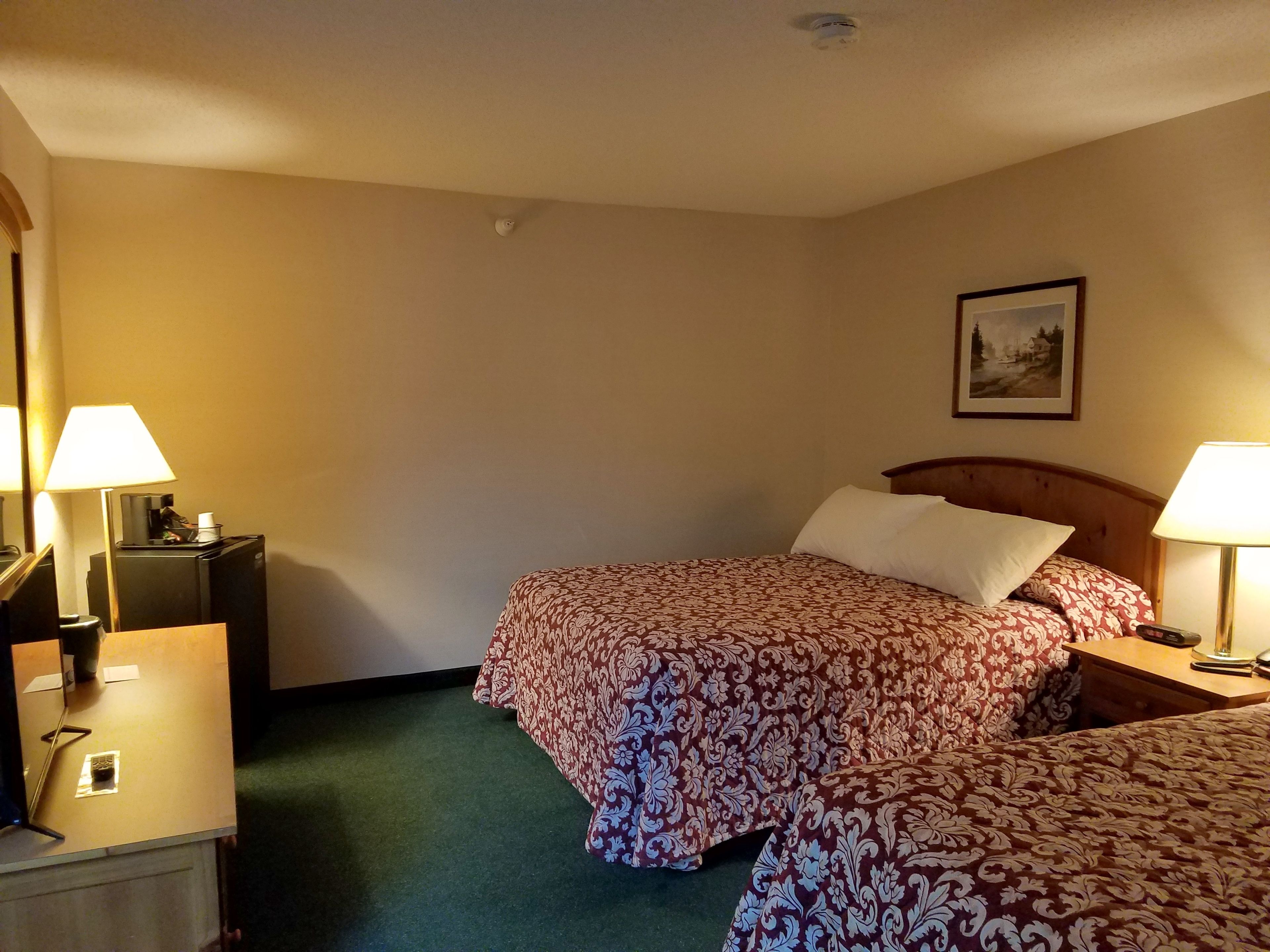 A hotel room with two beds, a desk, a chair, a lamp, and a picture on the wall.