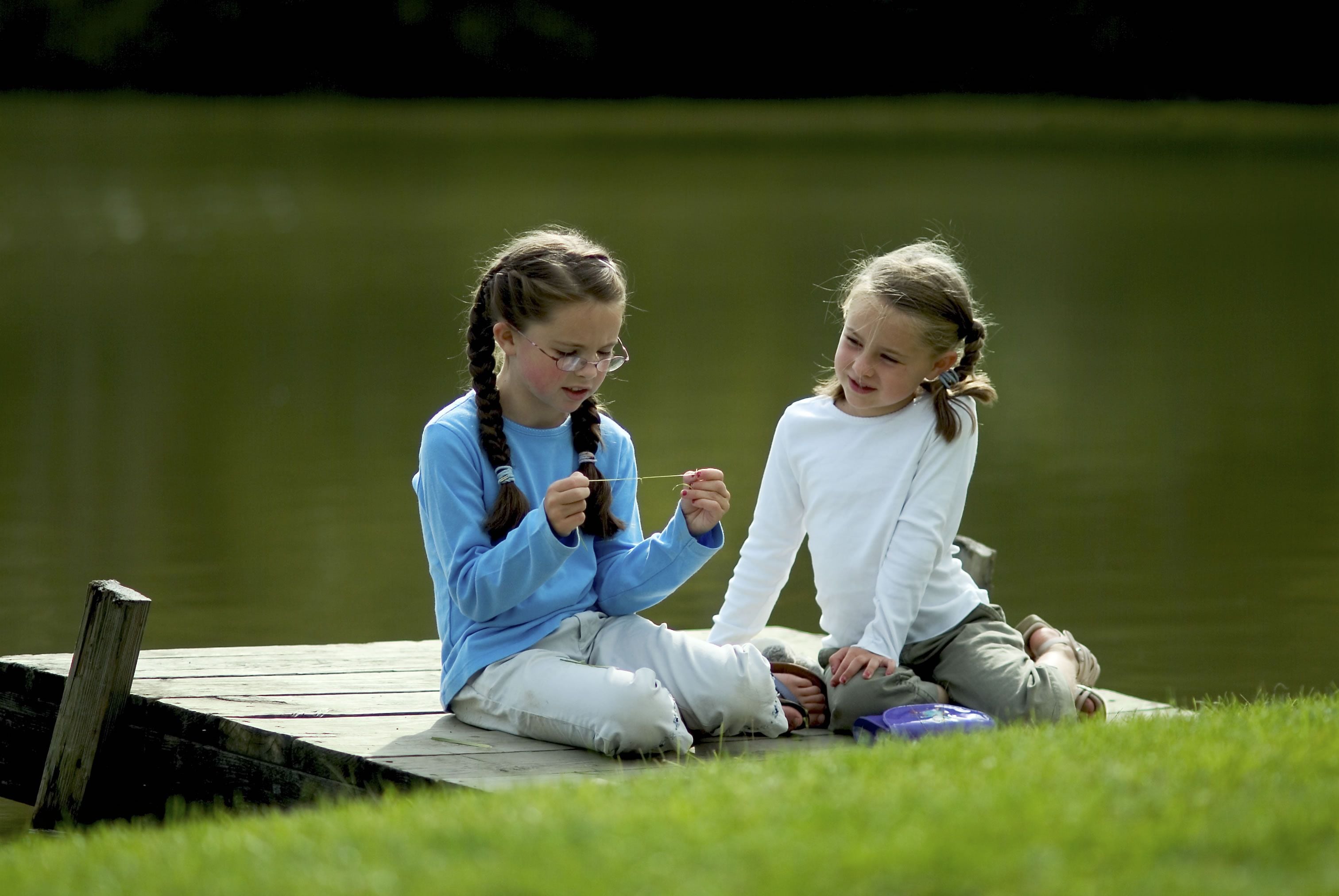 Two individuals sitting on a wooden dock by a body of water.