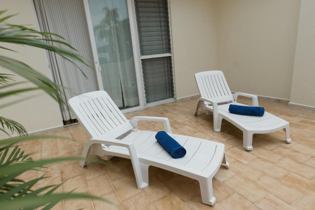 A balcony with three white plastic lounge chairs, each with a blue towel.
