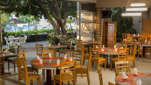 An indoor restaurant with round tables and wooden chairs, a TV mounted on the wall, and a view of the outdoors. - Gamma Cuernavaca Puerta Paraiso (Cuernavaca)