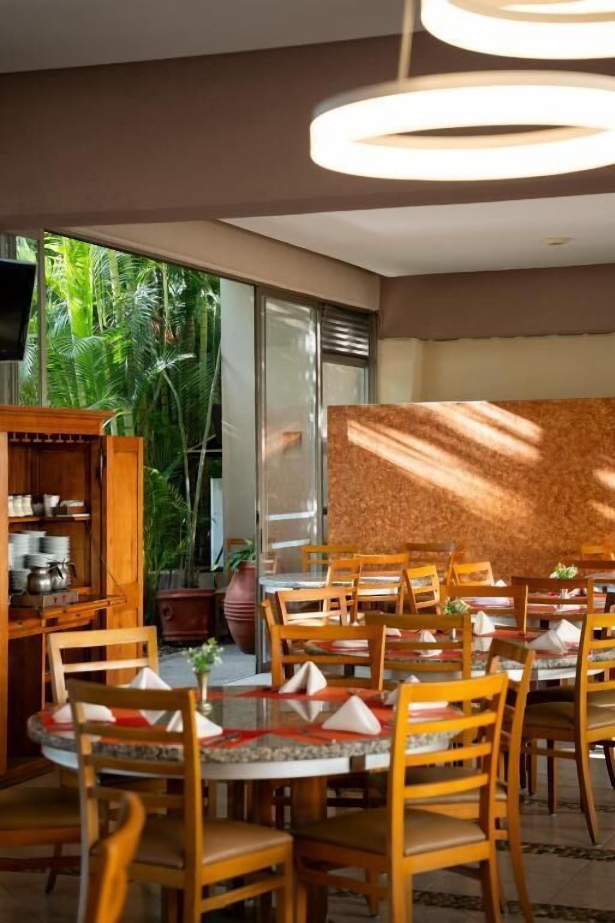 A dining area with round tables, wooden chairs, and a television on the wall.