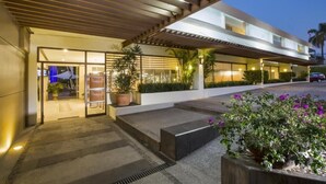 A modern hotel entrance with a covered walkway, potted plants, and a visible car in the background. - Gamma Cuernavaca Puerta Paraiso (Cuernavaca)
