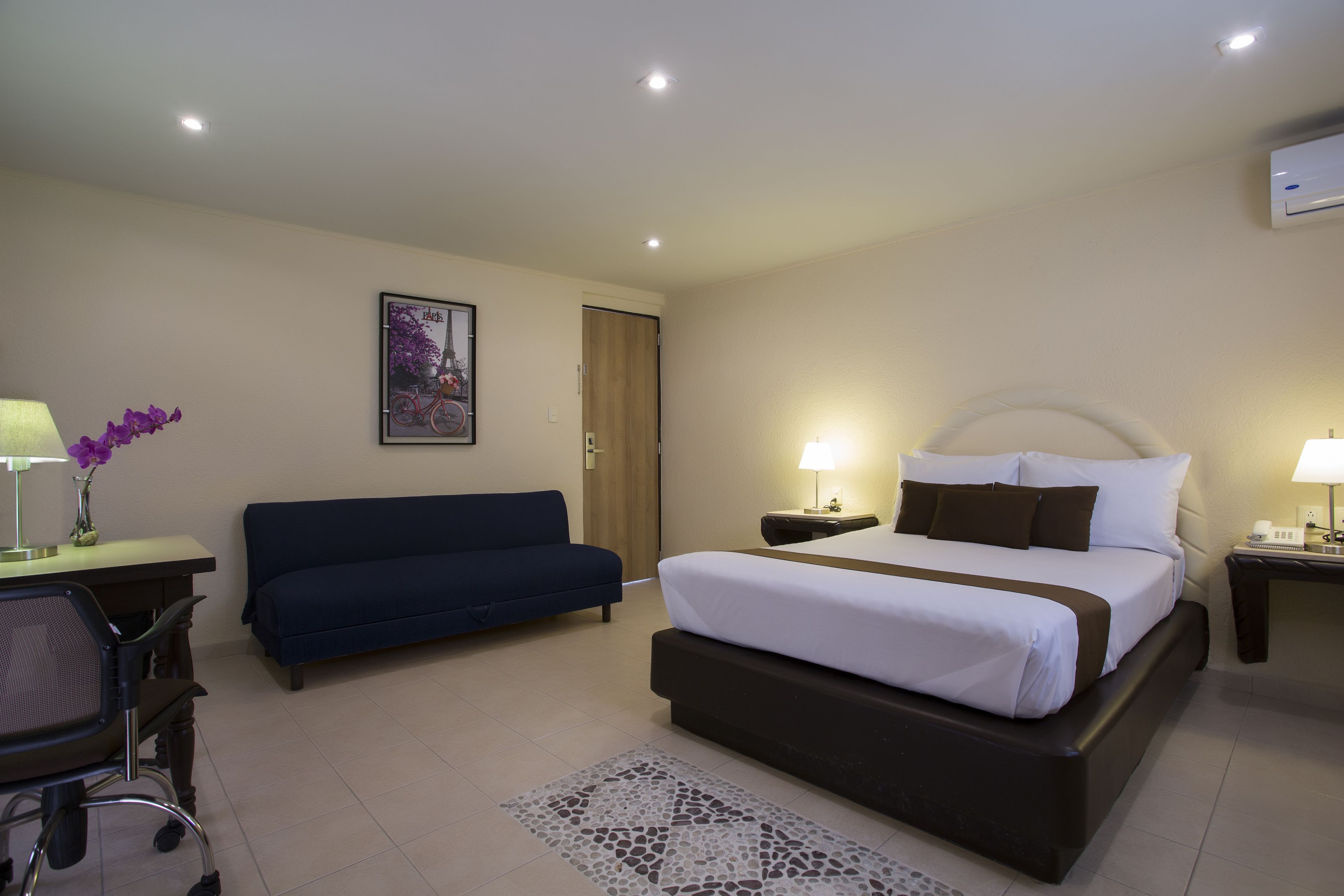 A hotel room with a bed, a desk with a chair, a sofa, and a picture on the wall.