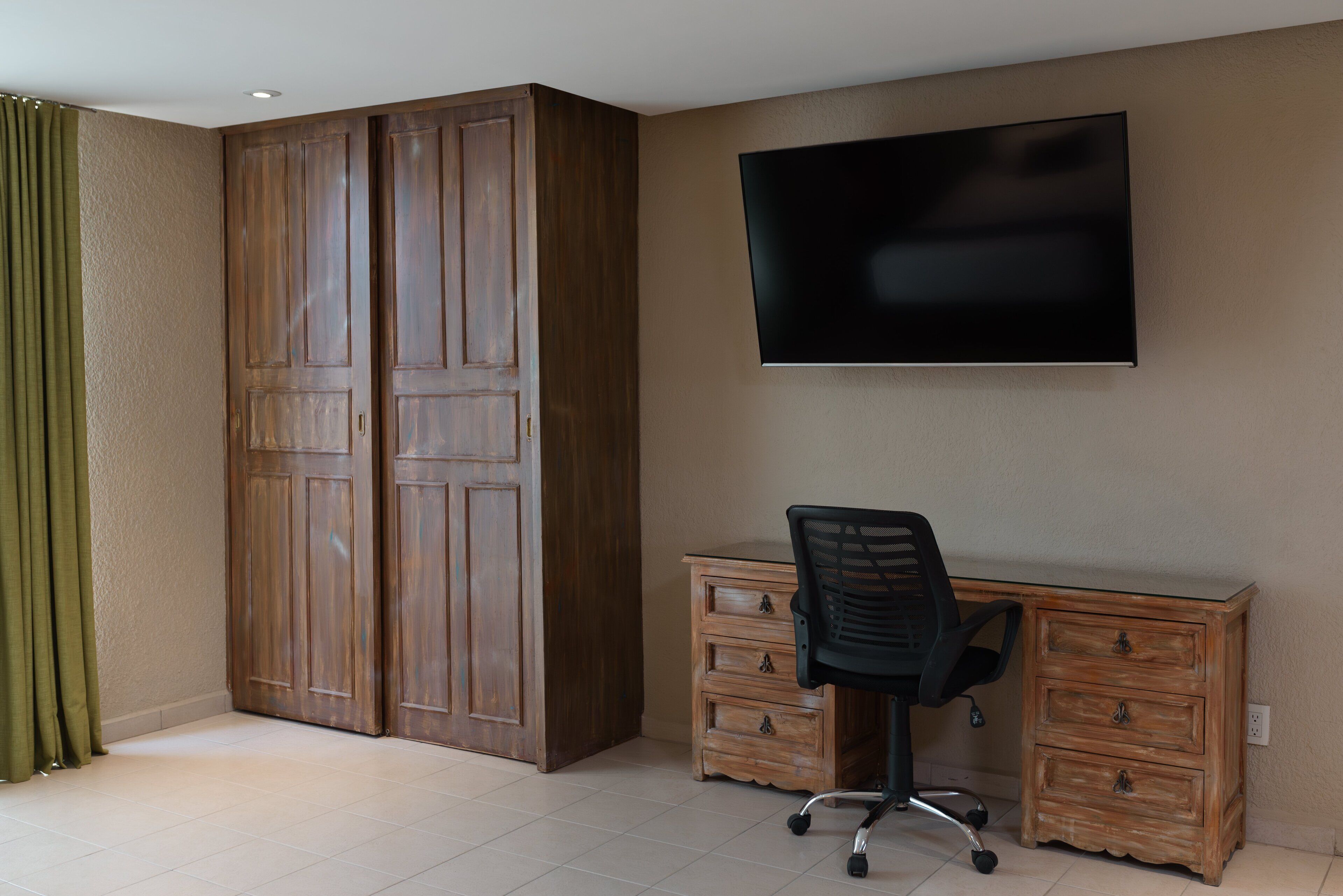 Une pièce comprenant une armoire en bois, un bureau avec des tiroirs, une chaise et un téléviseur à écran plat fixé au mur.