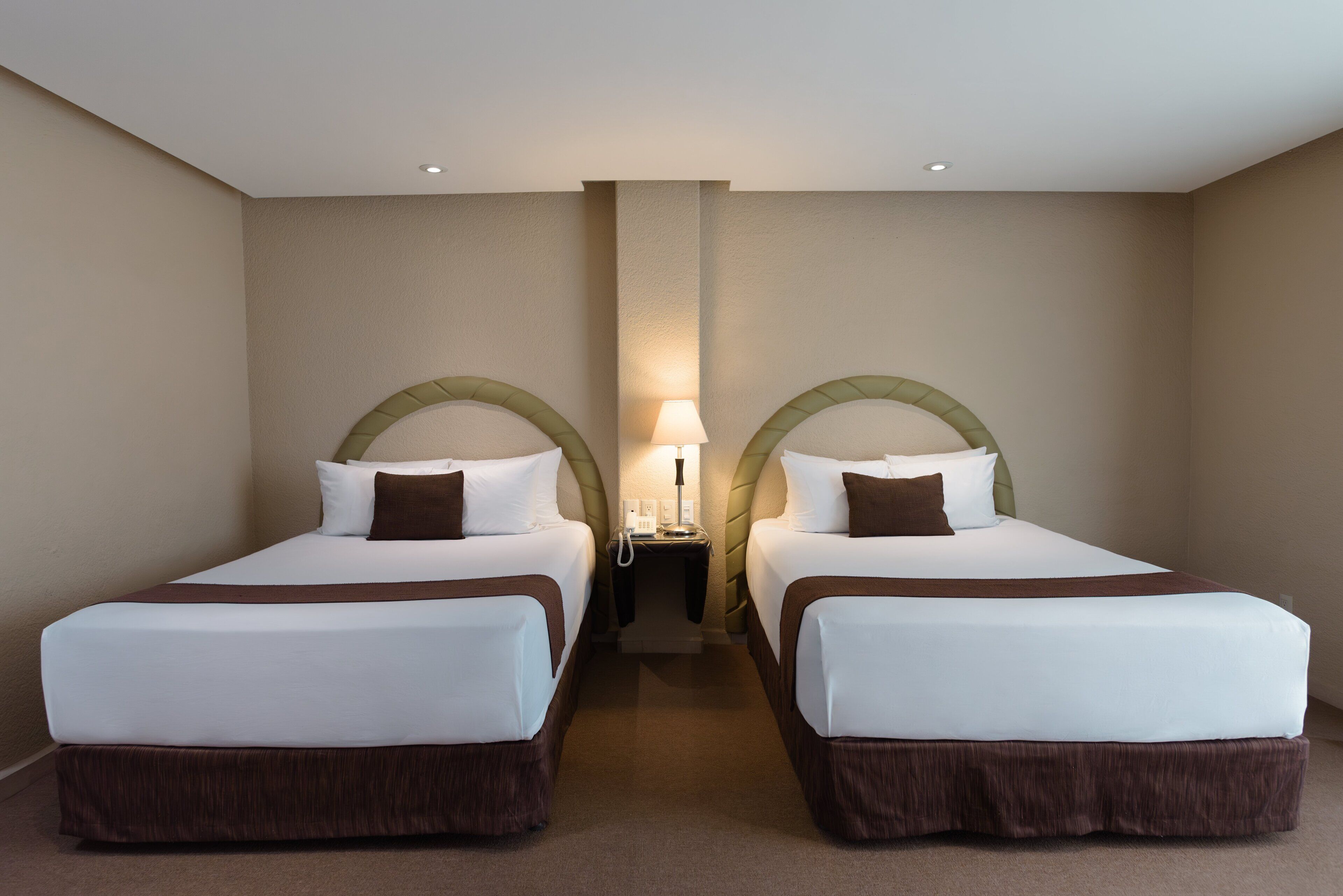Une chambre d’hôtel avec deux lits, une table de chevet et une lampe.