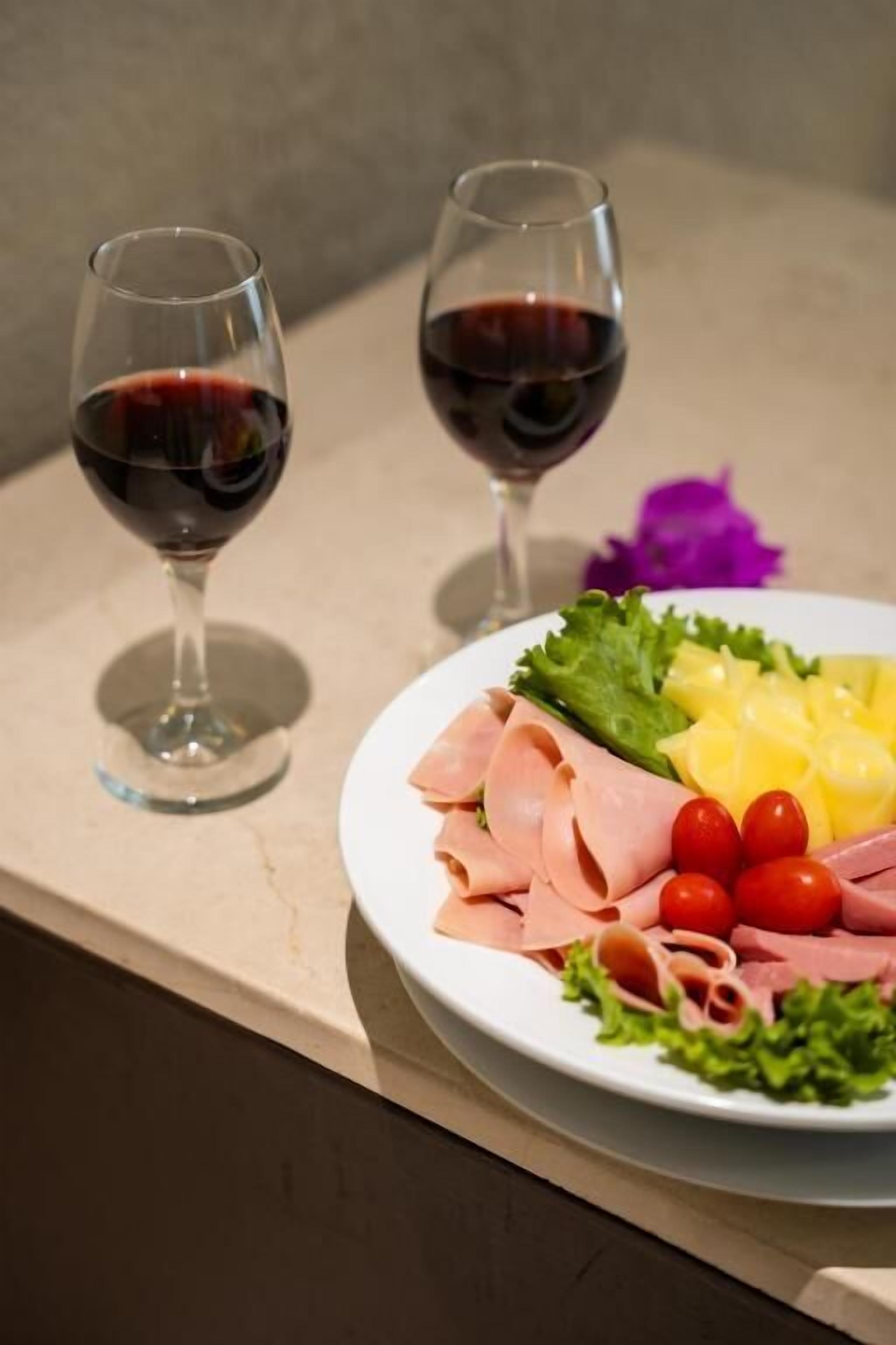 Un plato de embutidos y verduras sobre una mesa con dos copas de vino tinto.