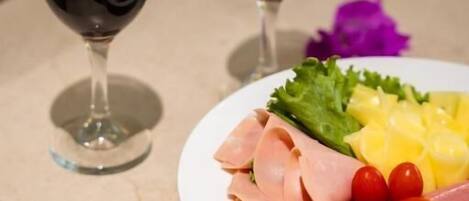 Un plato de embutidos y verduras sobre una mesa con dos copas de vino tinto.