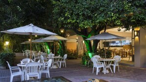 An outdoor dining area with white plastic chairs and tables, umbrellas, and a water feature. - Gamma Cuernavaca Puerta Paraiso (Cuernavaca)