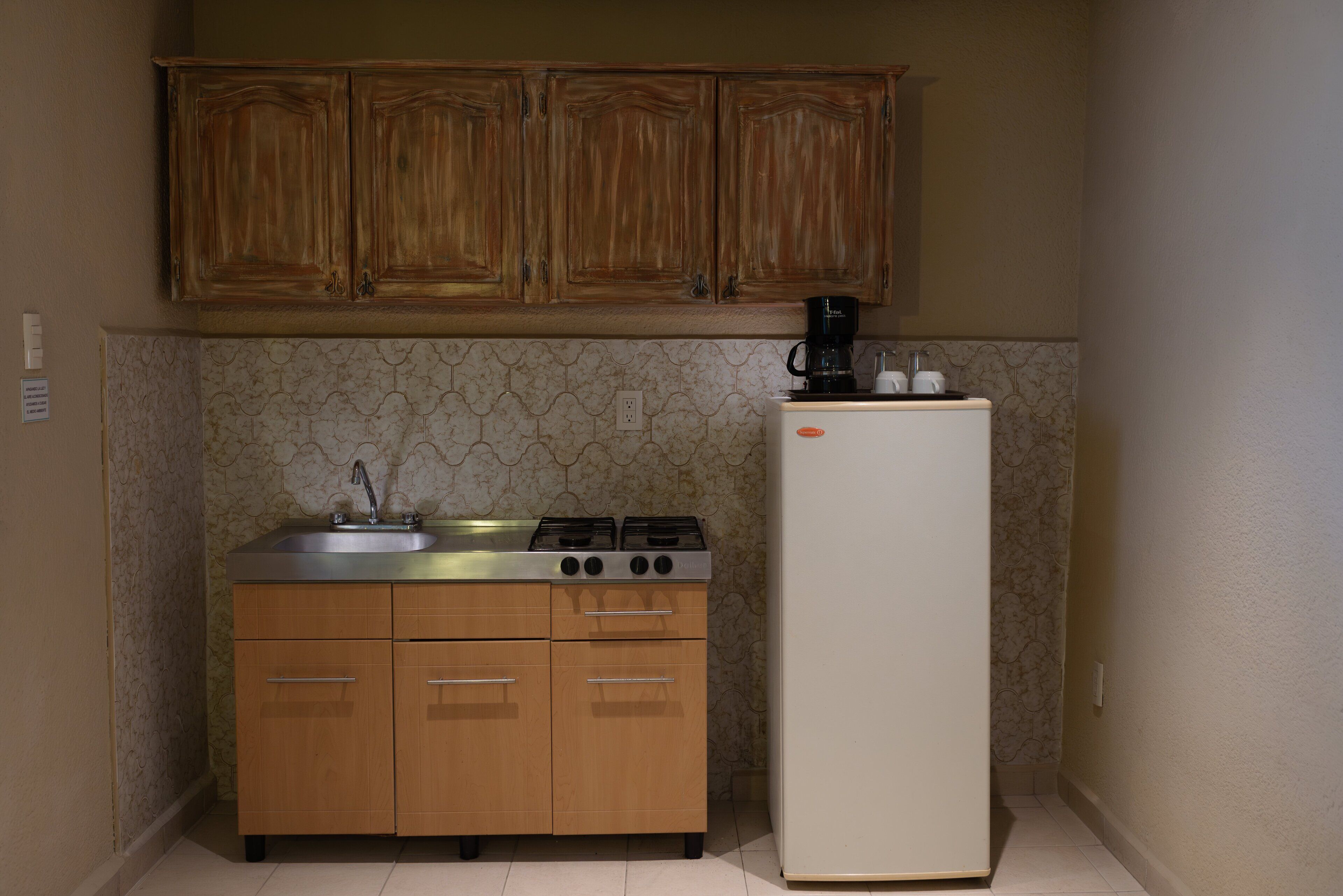 A compact kitchen with wooden cabinets, a stainless steel sink, a gas stove, and a white refrigerator.