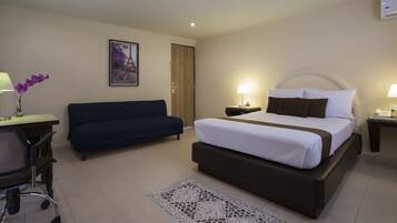 Quarto de hotel com cama, escrivaninha com luminária, cadeira, sofá e quadro na parede.