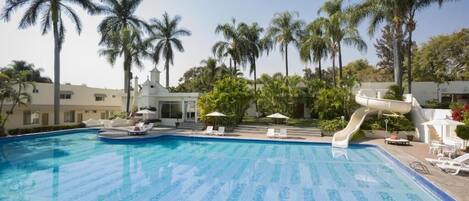 Una piscina con tobogán de agua, palmeras y sillas de descanso.