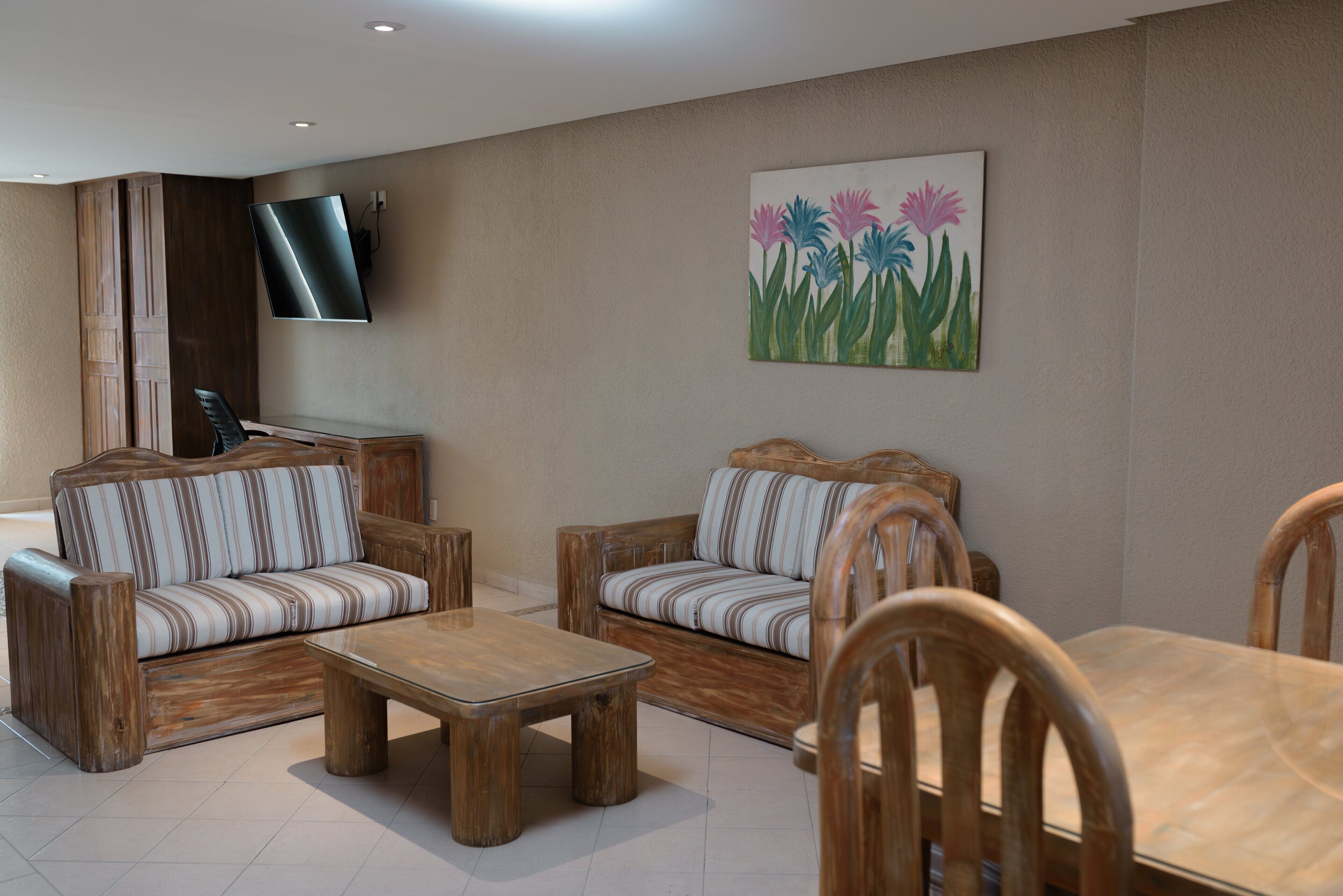 A modern living room with wooden furniture, a flat-screen TV, and a painting of flowers on the wall.