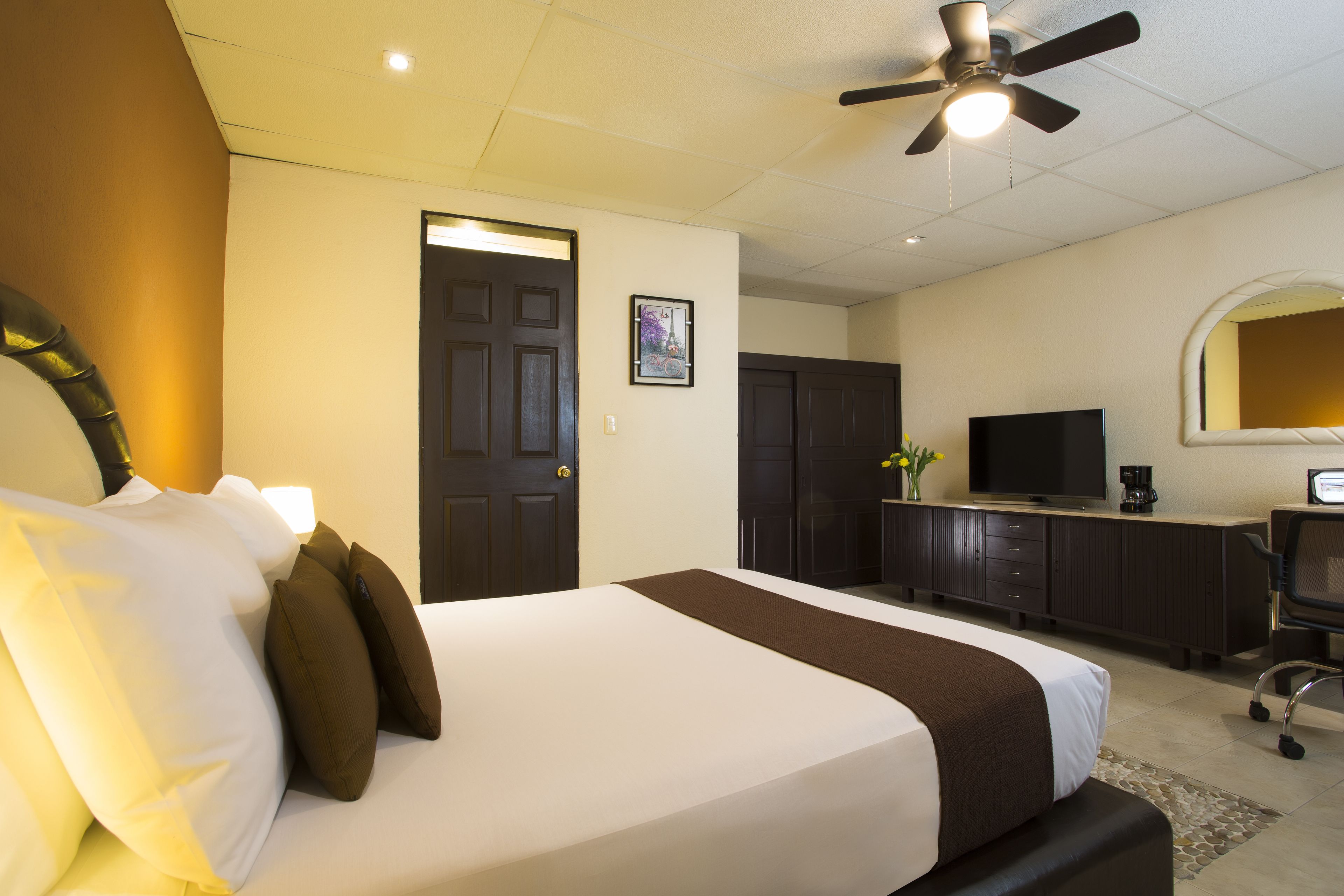 Ein Hotelzimmer mit Bett, Schreibtisch, Fernseher und Deckenventilator.
