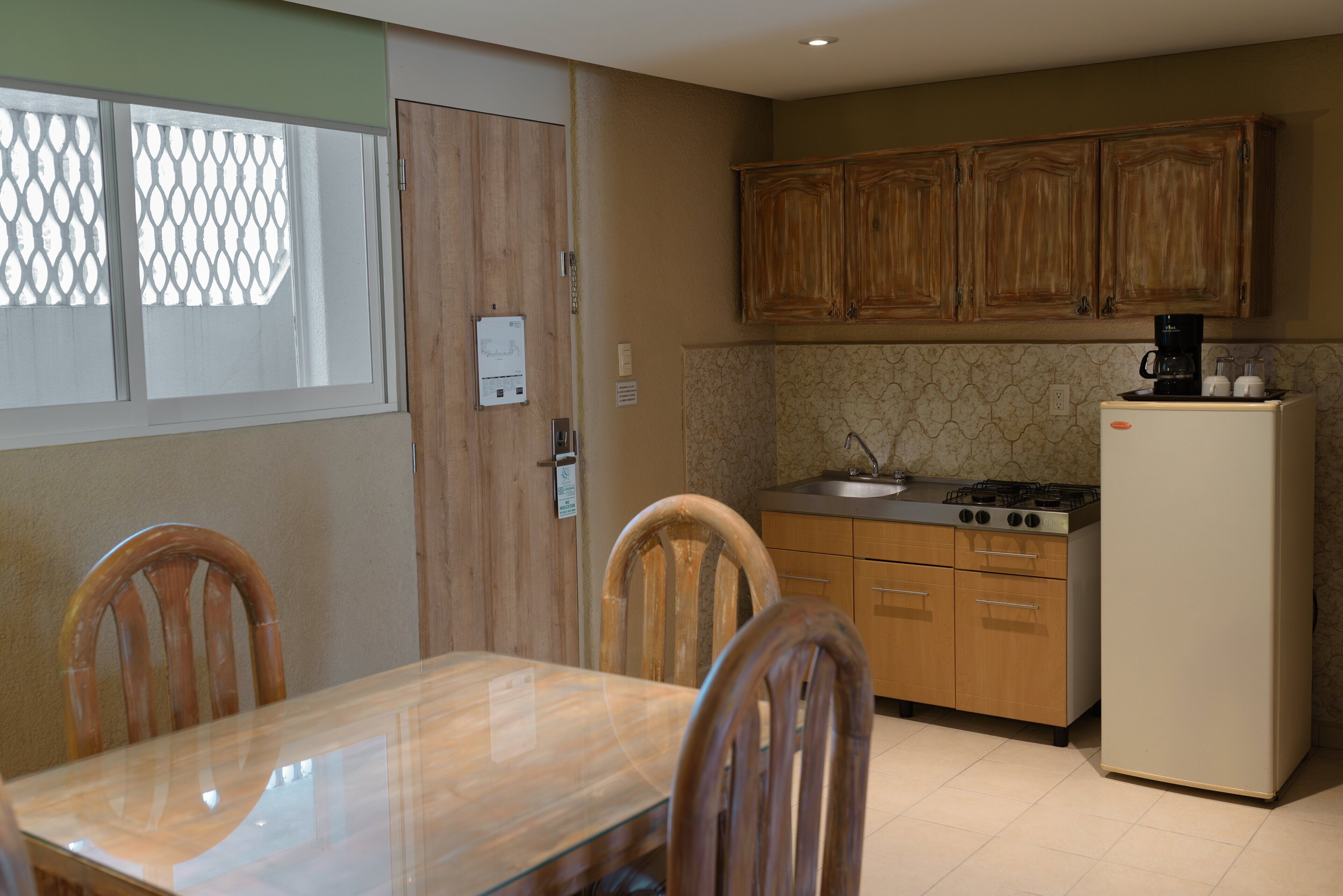 A compact kitchen with wooden cabinets, a gas stove, a refrigerator, and a dining table with chairs.