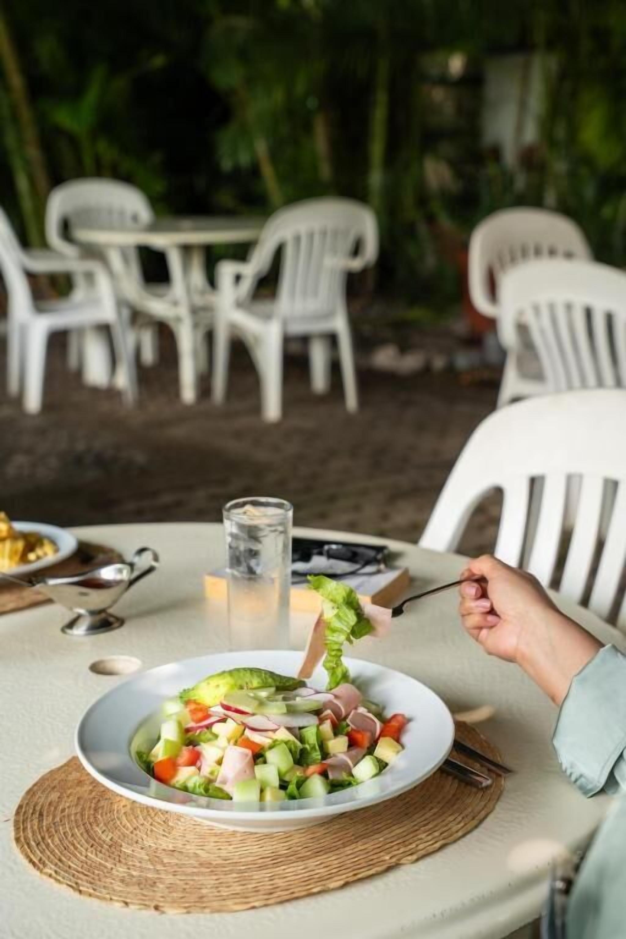 A dining table with a plate of salad, a glass of water, and a metal pitcher.