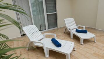 Un balcon avec deux chaises longues en plastique blanc, chacune agrémentée d’une serviette bleue roulée.
