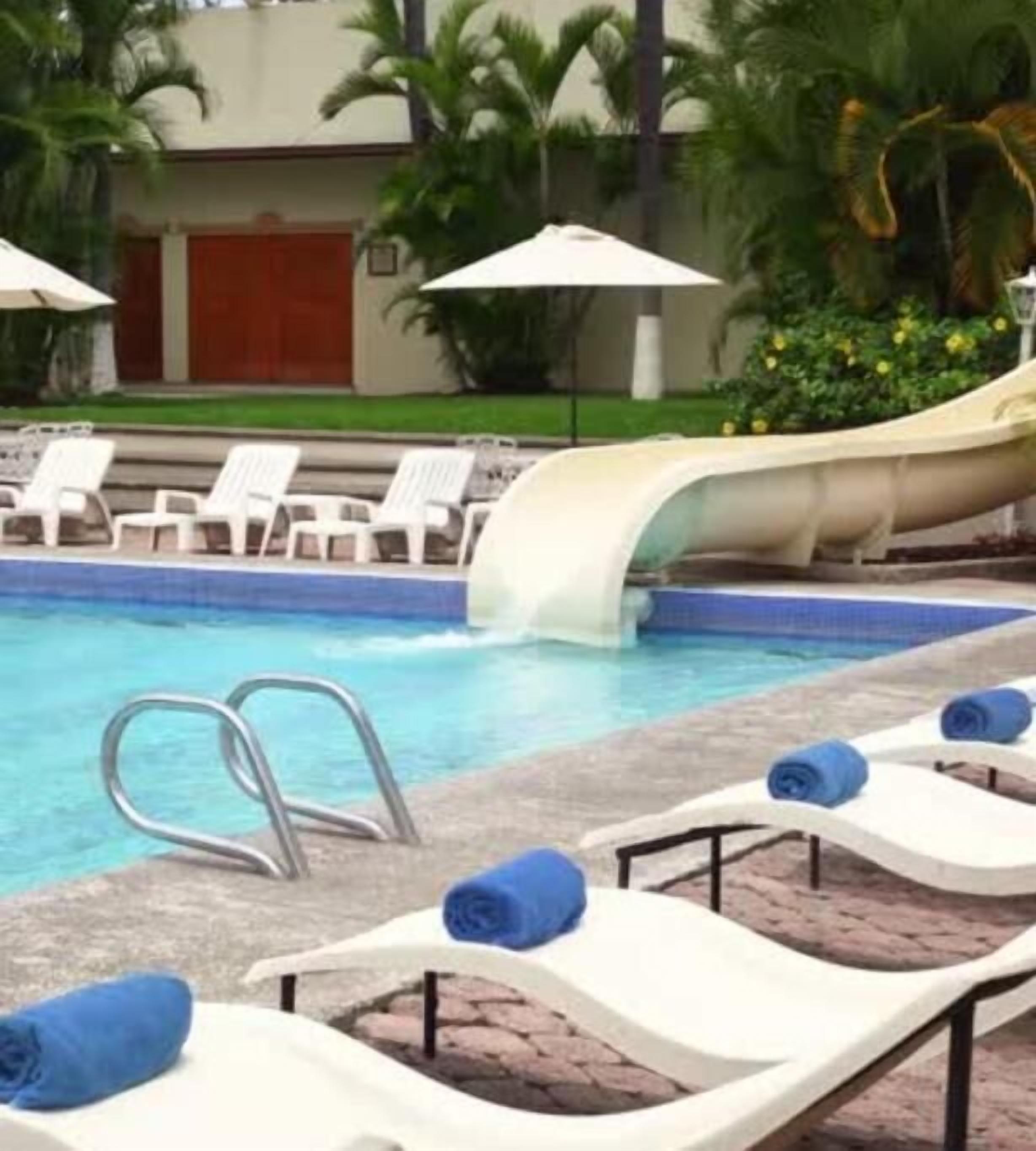 Una piscina con sillas de descanso y un tobogán de agua.