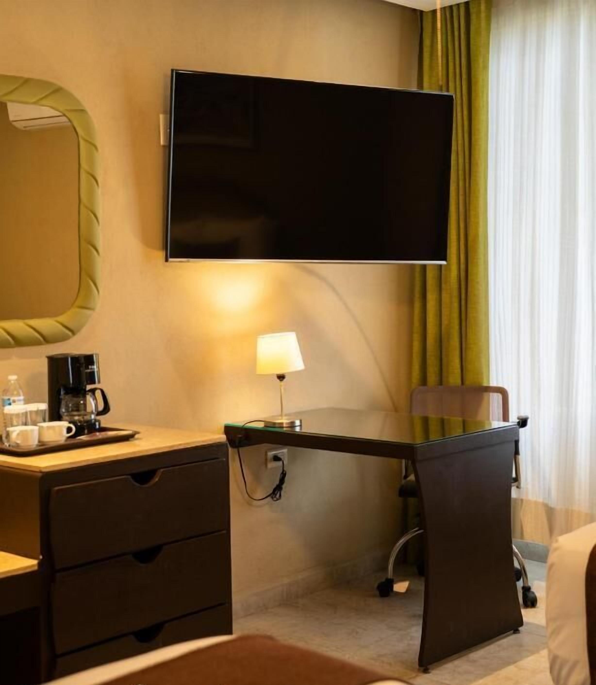 Une chambre d’hôtel équipée d’un bureau, d’une télévision à écran plat, d’une lampe, d’une machine à café et d’une chaise.