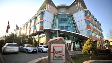A modern hotel building with a curved facade, multiple flags, and a sign indicating it is the MiDi Hotel.