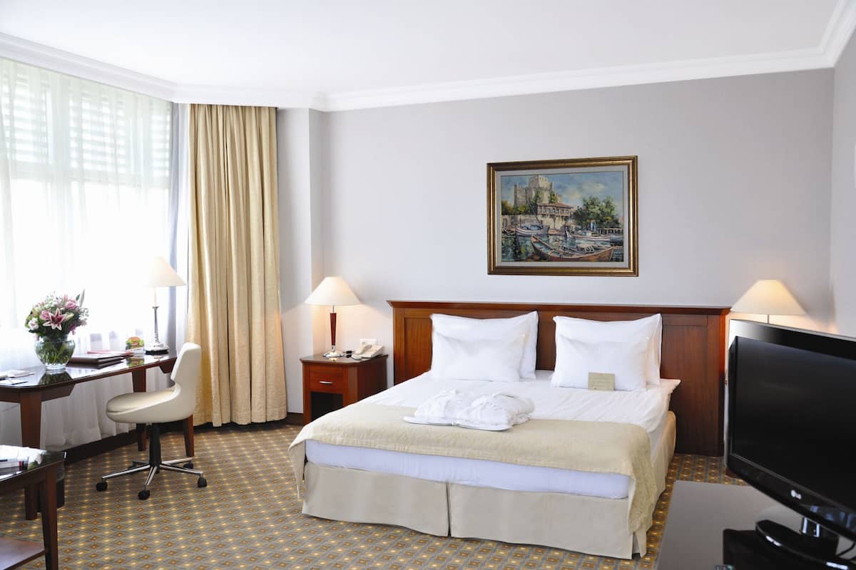 A hotel room with a bed, desk, chair, lamps, and a television.