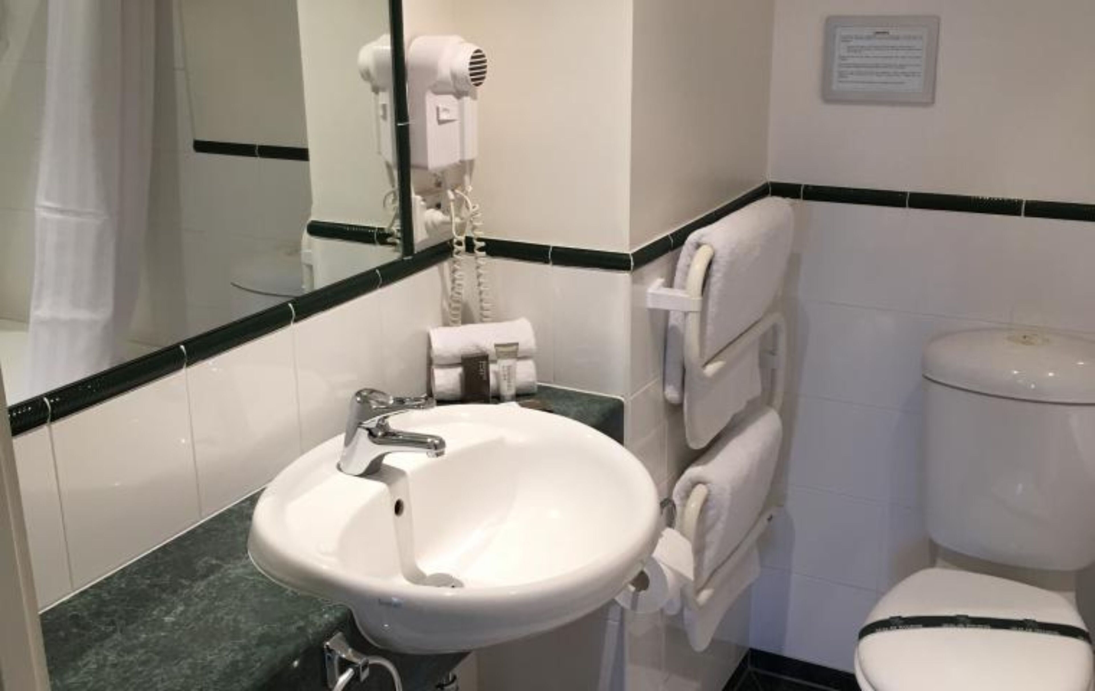 A bathroom with a white sink, a mirror, a hairdryer, and a toilet.