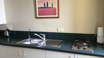 A kitchen with a stainless steel sink, a kettle, a stove, and a framed painting on the wall.