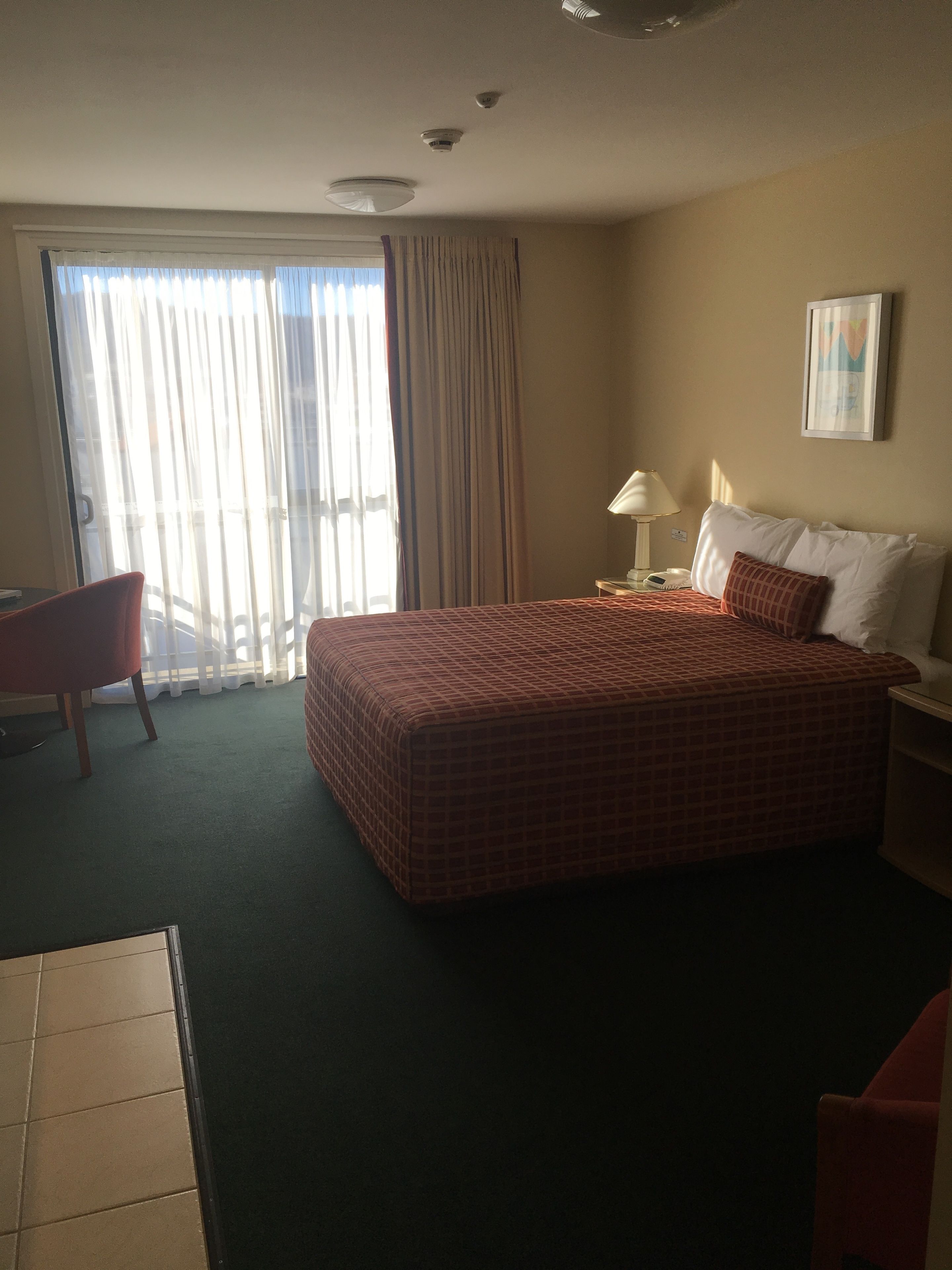 A hotel room with a large bed, a desk, a chair, a lamp, and a window with curtains.