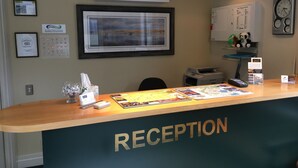 A reception desk with a framed landscape painting above it, a clock, and a smoke detector on the wall. - Motel on York (Dunedin)
