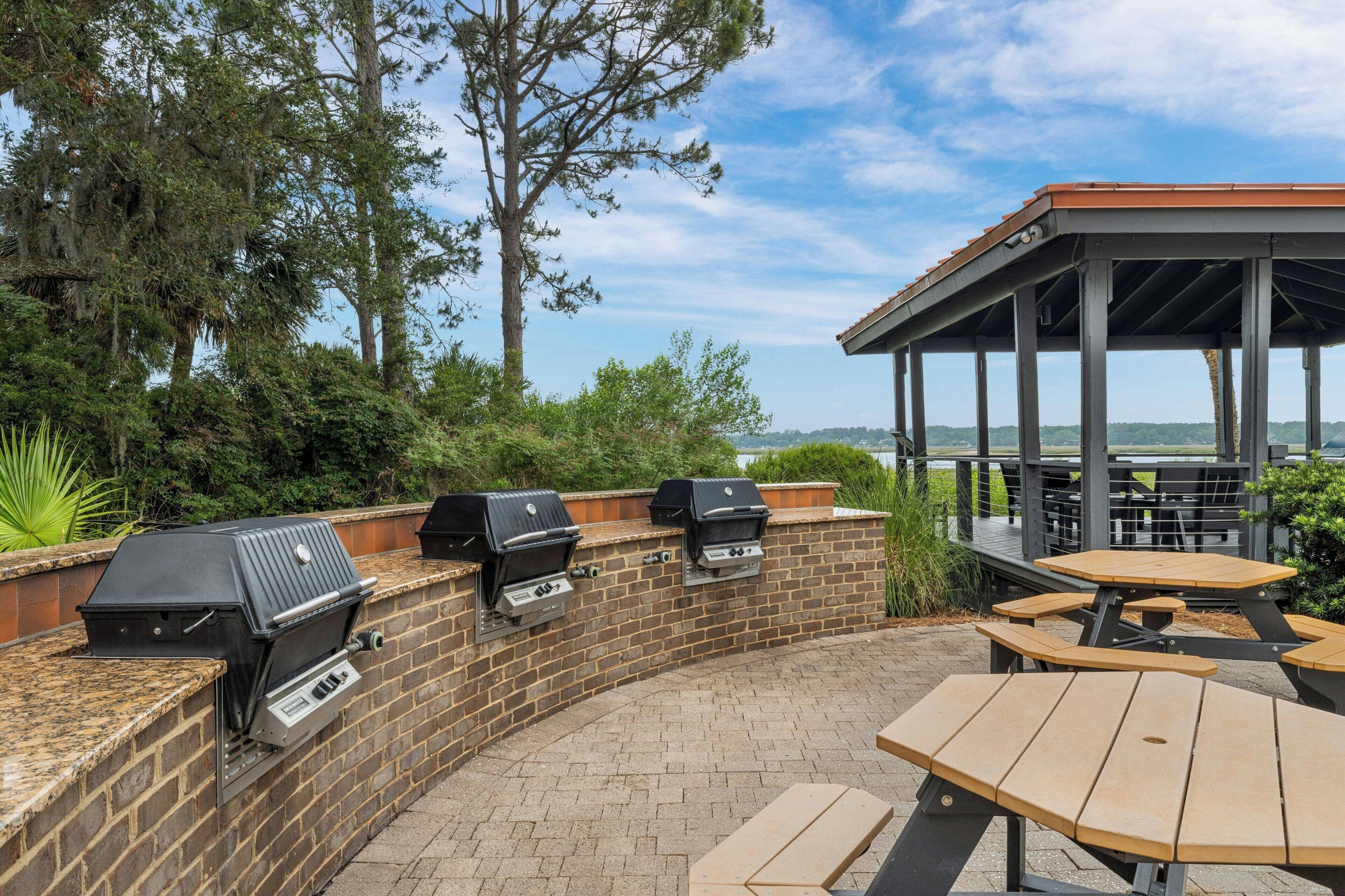 Une terrasse extérieure avec des murs en briques, deux barbecues à gaz, ainsi qu’une table et un banc en bois.