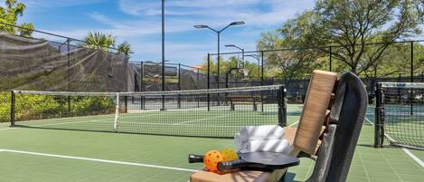 A tennis court with a bench, a towel, and sports balls.