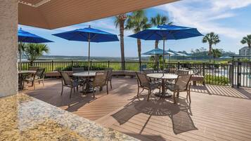 Une terrasse extérieure couverte, dotée de tables et de chaises, de parasols bleus et offrant une vue sur l’océan.