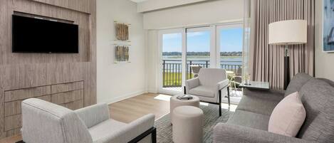 A modern living room with a flat-screen TV, grey sofas, a coffee table, and a balcony with a view.