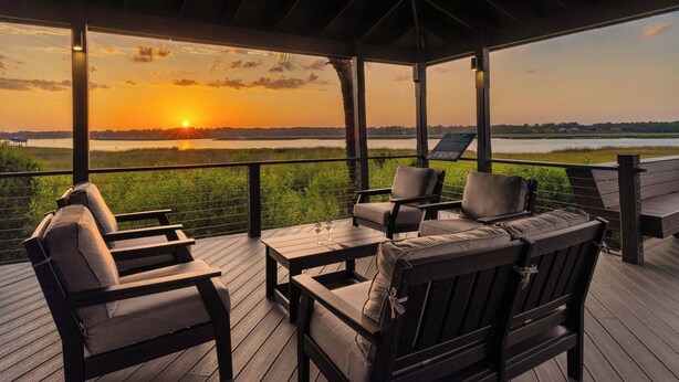 A covered outdoor seating area with a view of the sunset over a body of water.