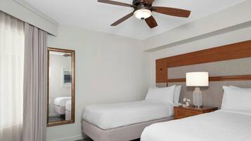 A hotel room with two beds, a ceiling fan, a nightstand with a lamp, and a large mirror.